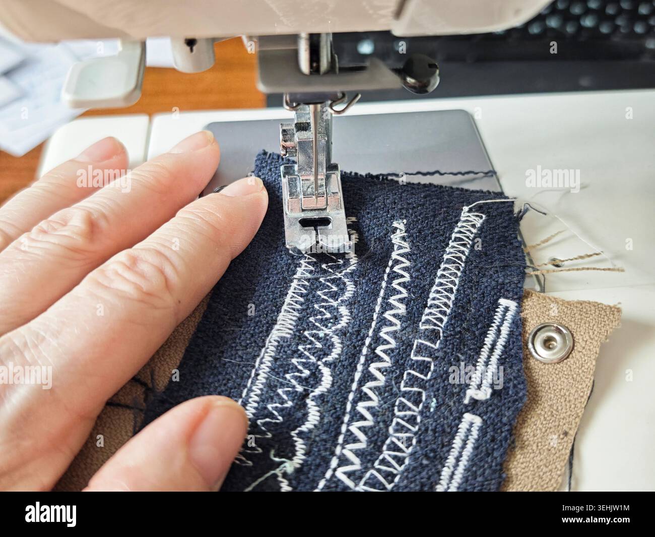 Une main tient le tissu près d'une machine à coudre car elle coud différents motifs sur le matériau dans un espace de travail pendant la journée. Banque D'Images