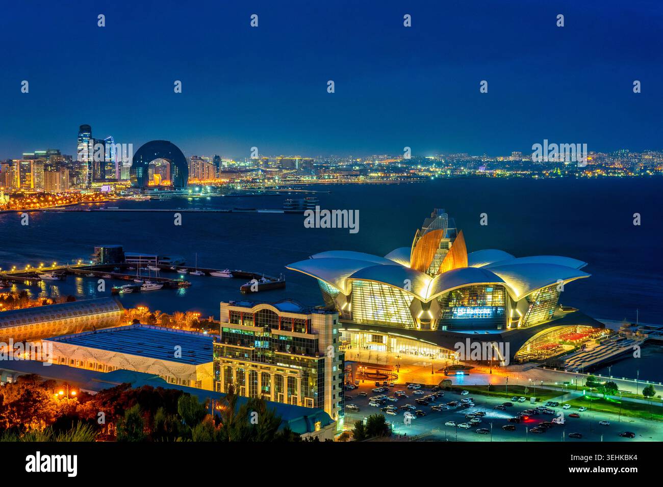 Bâtiment en forme de lotus du centre commercial Deniz Mall illuminé la nuit sur le front de mer Caspienne, avec Port Baku Crescent au-delà. Bakou, Azerbaïdjan. Banque D'Images