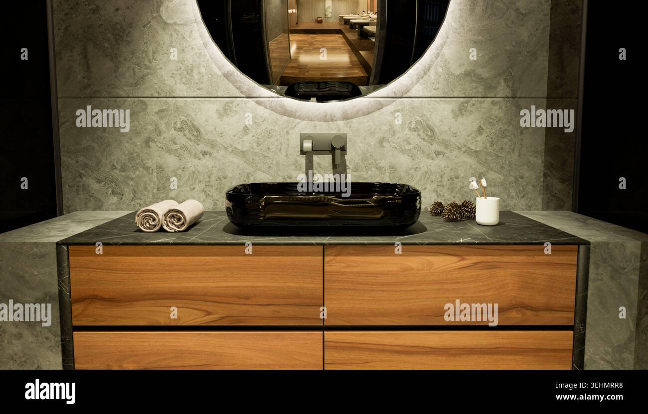 Salle de bains moderne de luxe avec meuble-lavabo en bois, évier en pierre noire, miroir rond et décoration minimaliste. Un éclairage chaleureux et des lignes épurées créent Banque D'Images