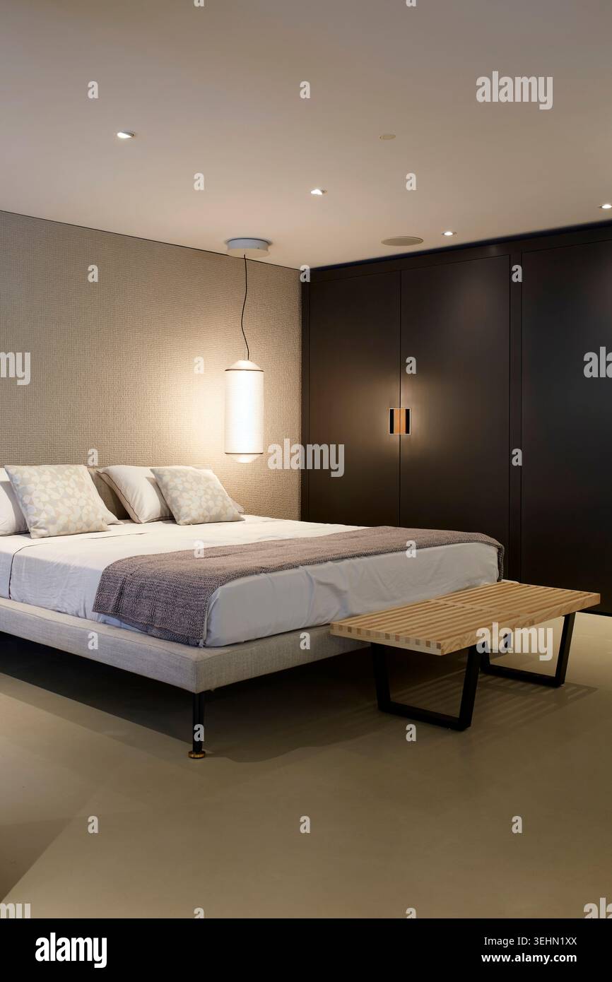 Intérieur de chambre minimaliste moderne avec lit soigneusement fait, textiles neutres doux, lumière suspendue et armoire intégrée sombre, mettant en vedette l'élégante maison sta Banque D'Images