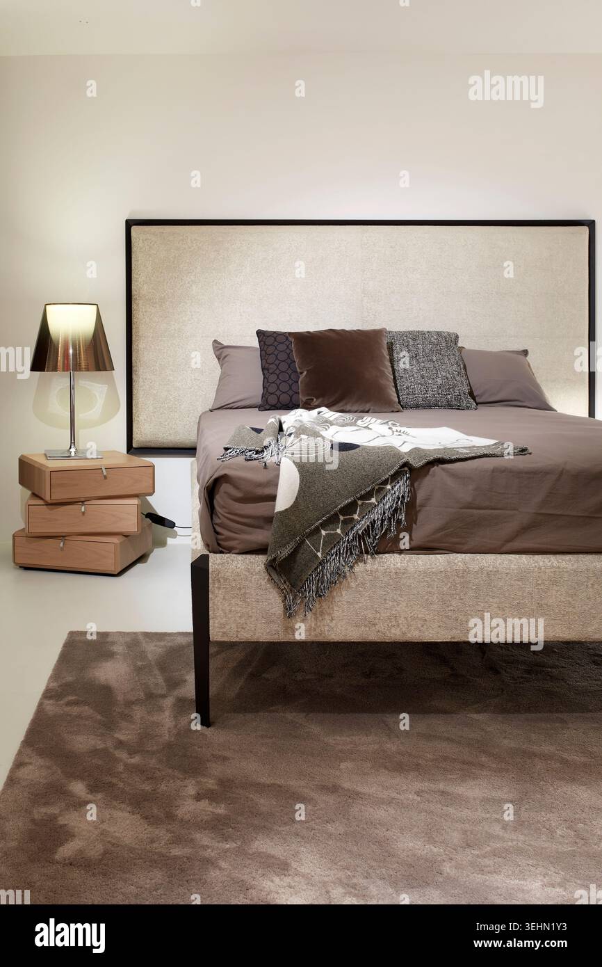 Intérieur contemporain de la chambre avec lit rembourré, literie neutre, jeté texturé, lampe de chevet et table de chevet, décor minimaliste et tapis moelleux, idéal pour fo Banque D'Images