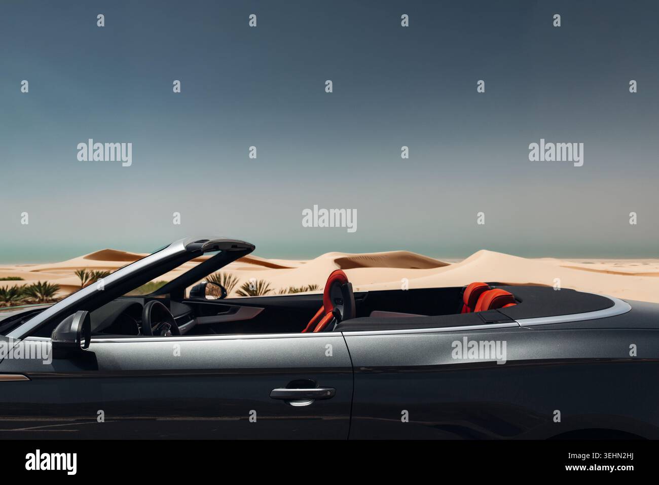 Voiture décapotable de luxe élégante avec toit ouvert garée près des dunes dorées du désert sous un ciel dégagé, capturant un sentiment de liberté, de voyage et de route élégante Banque D'Images