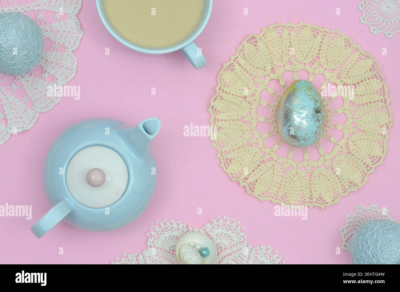 Couleurs pastel sur la table : décoration de Pâques avec œufs de Pâques bleus, dentelle, jaune, serviette vintage, tasse de café et théière bleue sur table rose. Banque D'Images