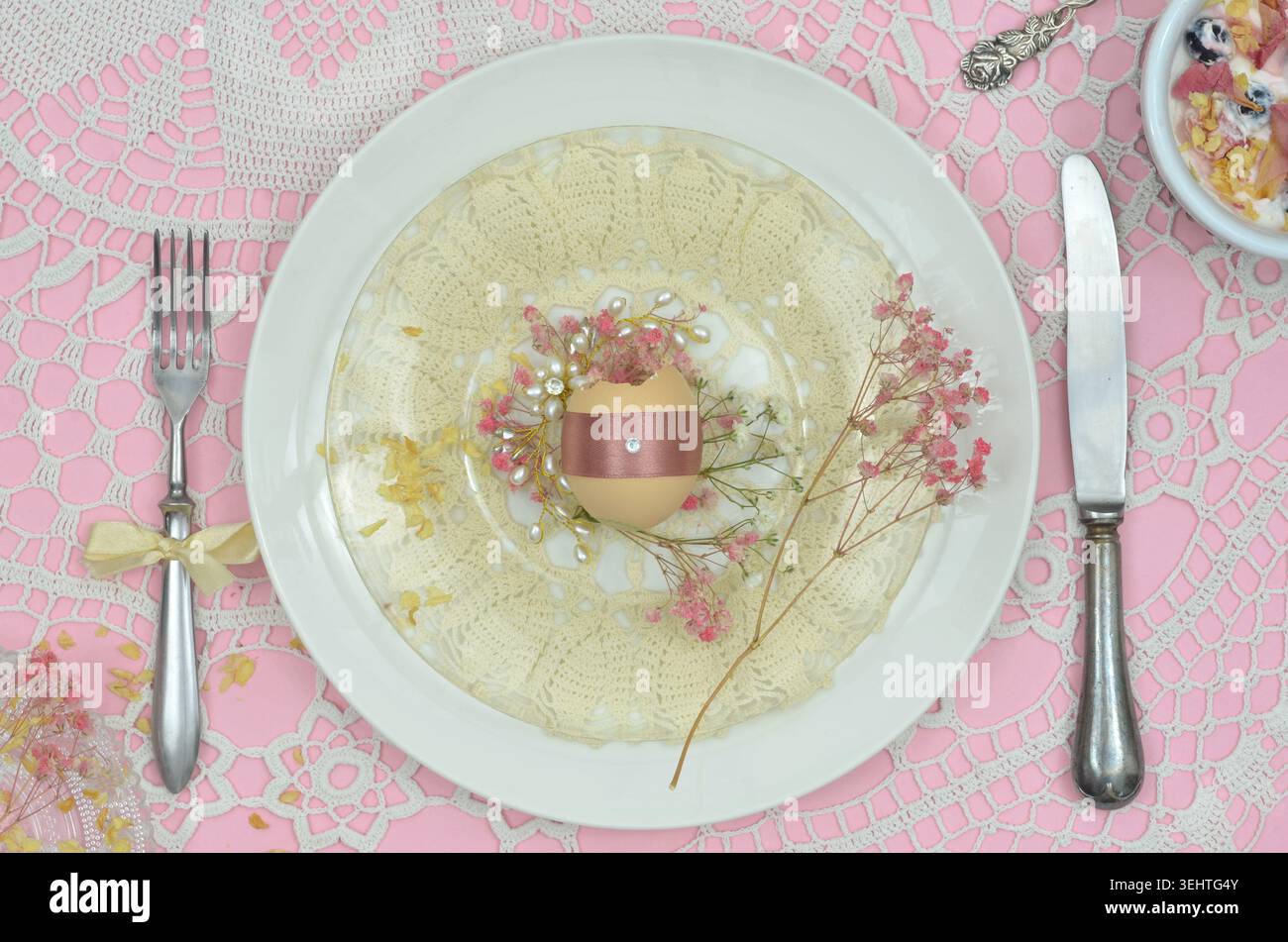 Table pour Pâques : vue de dessus décorations élégantes : serviette crochetée jaune, fond rose, oeuf de Pâques sur assiette blanche, fourchette rétro et couteau. Banque D'Images