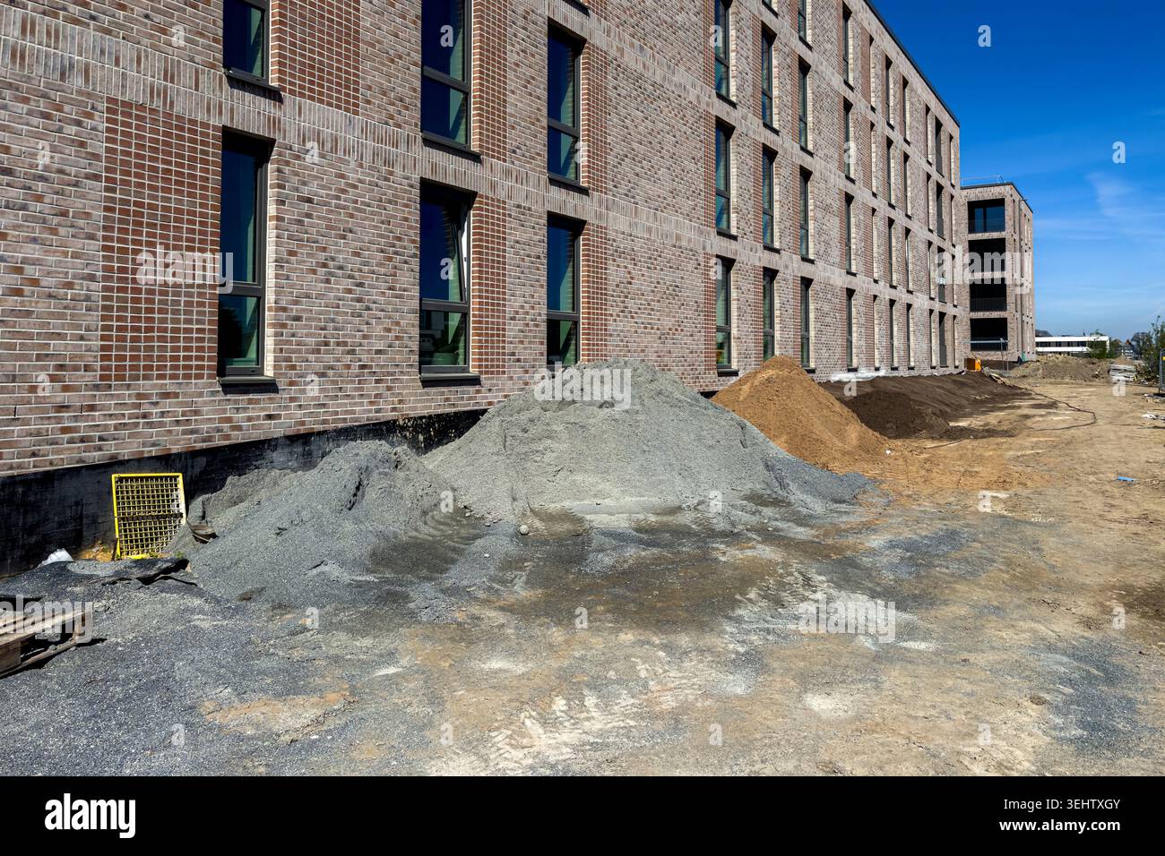 Les ouvriers préparent le site pour un nouveau bâtiment. Des tas de sable, de gravier et de saleté sont présents sur le sol. Le ciel est clair et bleu. La construction est en place Banque D'Images