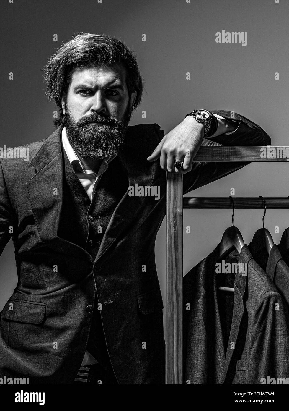Costume. Costumes masculins suspendus dans une rangée. Tailleur dans son atelier, designer. Homme barbu en costume. Noir et blanc Banque D'Images