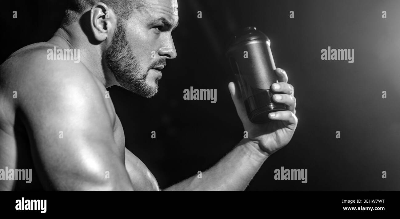 Boissons de l'eau dans la salle de gym. Homme au gymnase et tenant une bouteille d'eau. Homme musclé buvant de l'eau. Noir et blanc Banque D'Images