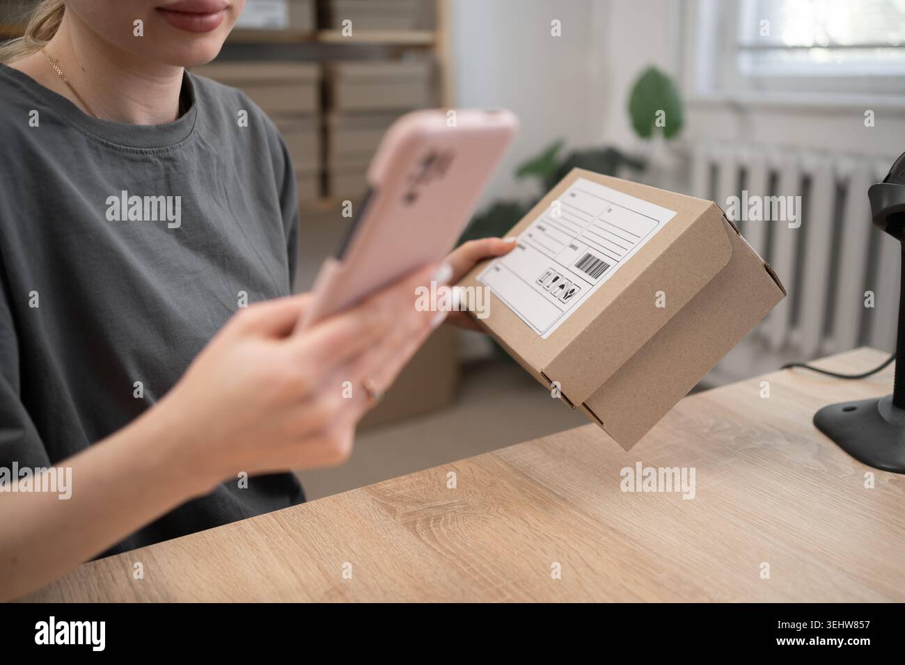Femme ouvrière d'entrepôt tenant la boîte et le téléphone préparant la chaîne d'approvisionnement dans le bureau de distribution pour le balayage de code à barres. logistique pour la livraison. Gros plan Banque D'Images