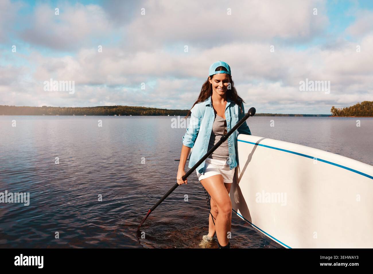 Femme, paddle board et vacances au lac avec le sourire, les loisirs et l'espace avec équipement en été. Personne, heureux et en plein air avec escapade touristique Banque D'Images