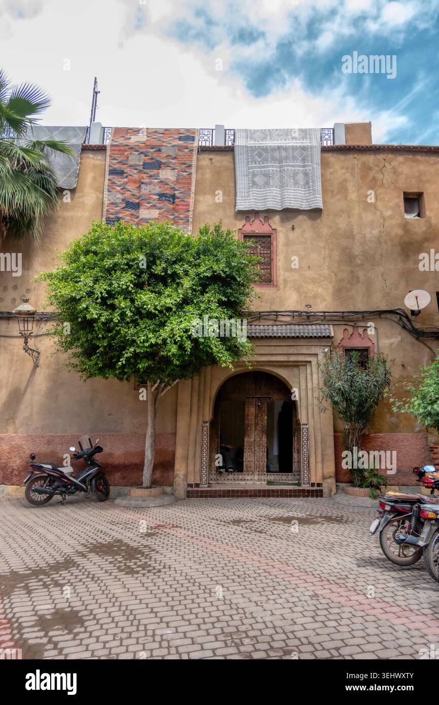 Bâtiment marocain traditionnel avec une porte en bois voûtée, des tapis suspendus au toit et un scooter garé dans une rue pavée Banque D'Images