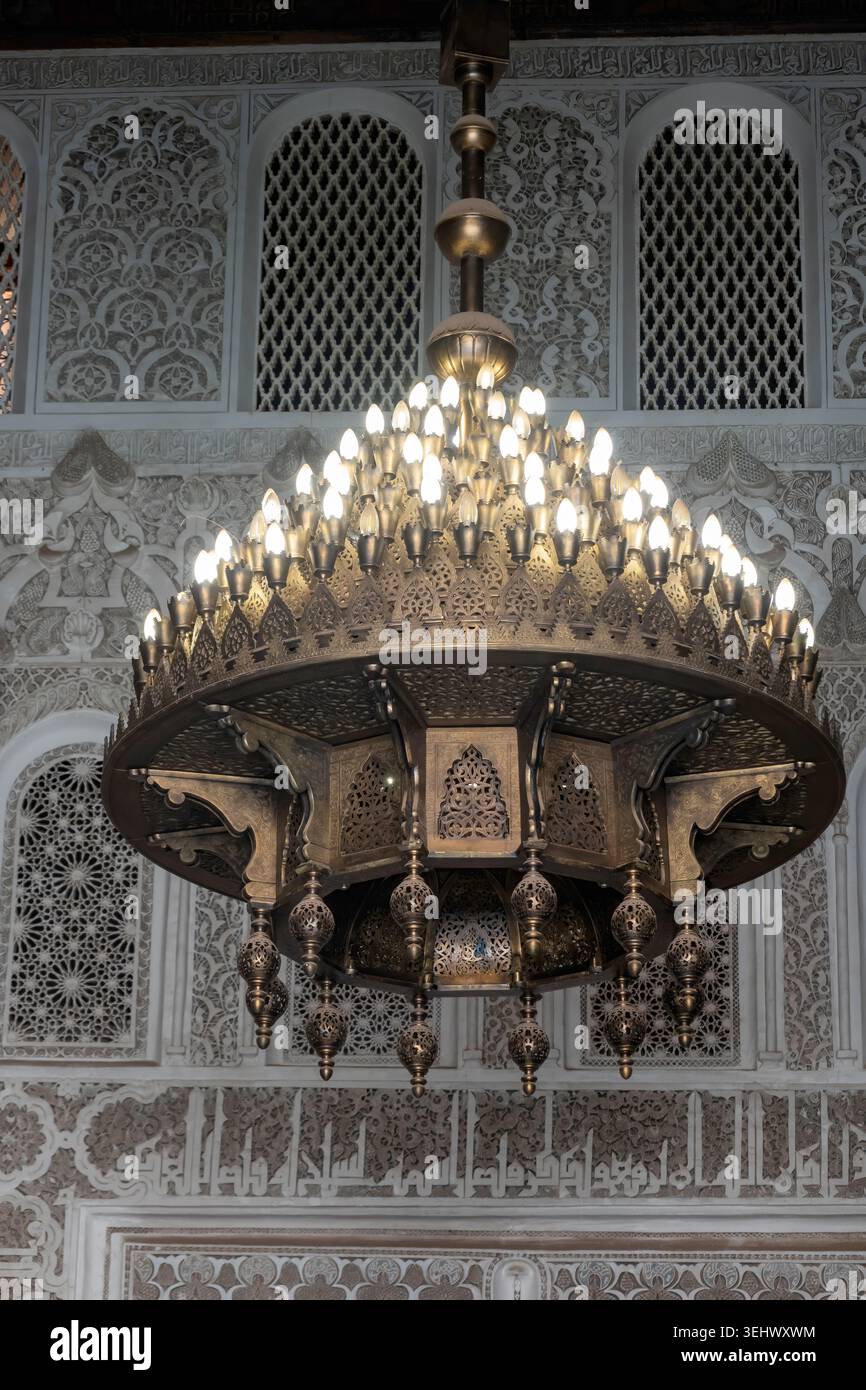 Lustre marocain orné en laiton illuminé sur un fond de sculptures complexes en stuc islamique et de calligraphie arabe dans un palais historique. Banque D'Images