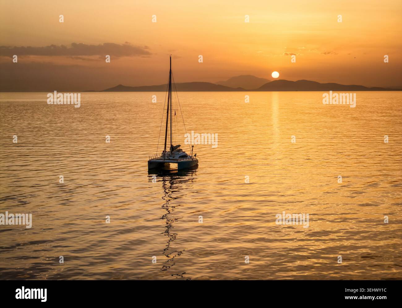 Une silhouette d'un voilier catamaran sur l'océan calme lors d'un coucher de soleil doré dans la mer méditerranée, en Grèce, en arrière-plan Banque D'Images