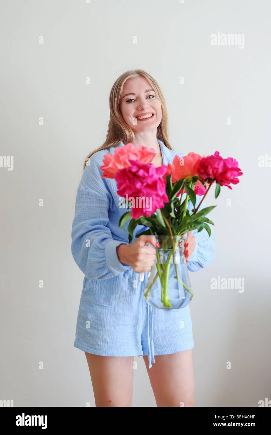 Femme blonde heureuse avec bouquet de pivoine coloré dans un studio lumineux, beauté féminine et concept de soins personnels avec lumière naturelle. Banque D'Images