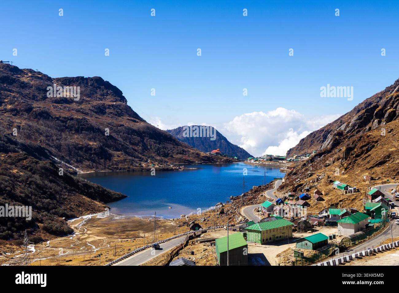 Vue panoramique à grand angle du lac Tsomgo entouré de montagnes rocheuses, d'une autoroute sinueuse et d'un village touristique au bord du lac, Sikkim, Inde. Banque D'Images