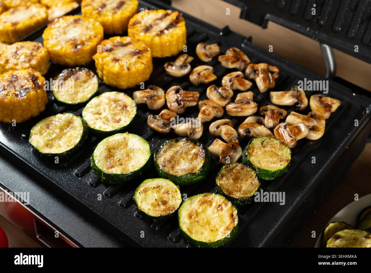 Cuisson du maïs, de la courgette et des champignons ensemble sur la plaque Home Grill Banque D'Images