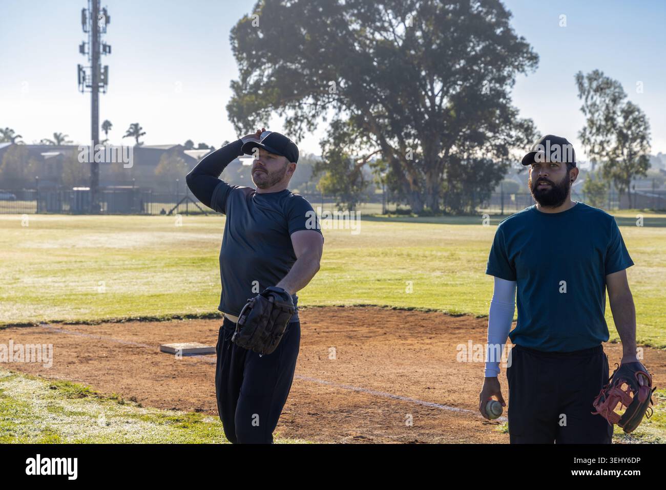 Deux joueurs masculins debout sur le terrain près de la plaque, ajustant la casquette et tenant le baseball, portant des gants Banque D'Images