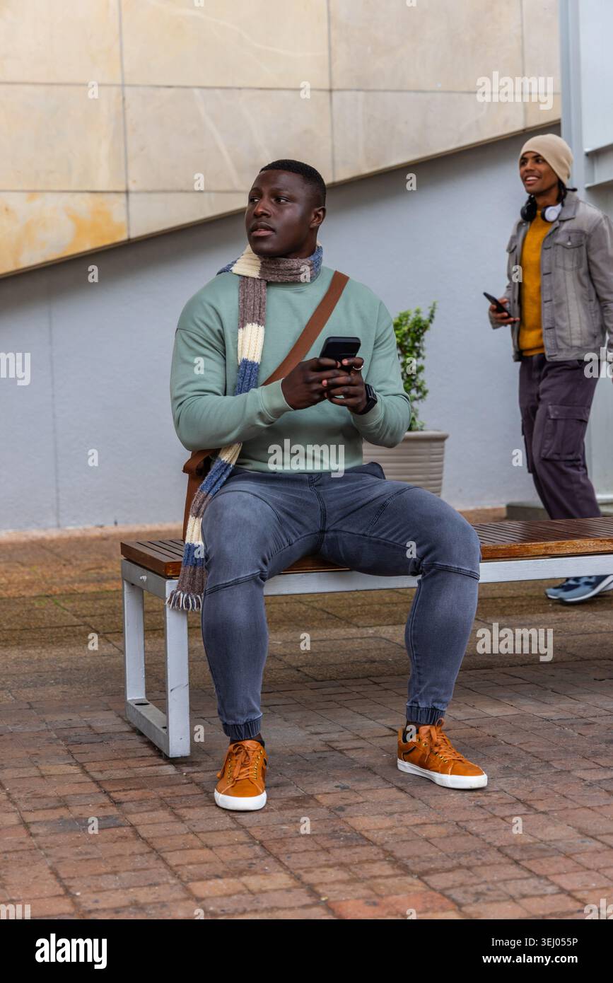 Divers piétons masculins assis sur le banc et passant devant la plaza, tenant des smartphones Banque D'Images