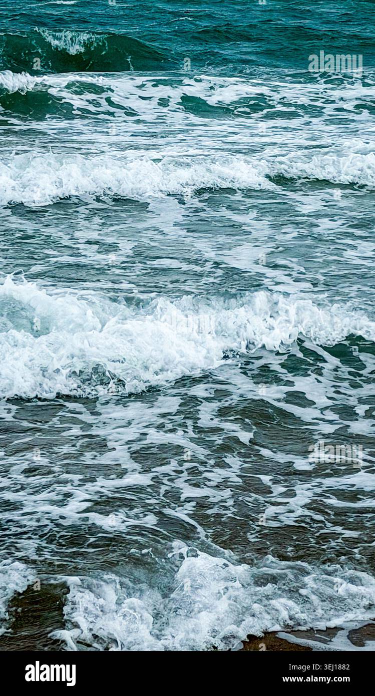 Les vagues de l'océan s'écrasent sur la plage de sable avec du surf blanc mousseux et de l'eau turquoise créant une scène côtière dynamique dans des conditions d'éclairage naturel Banque D'Images