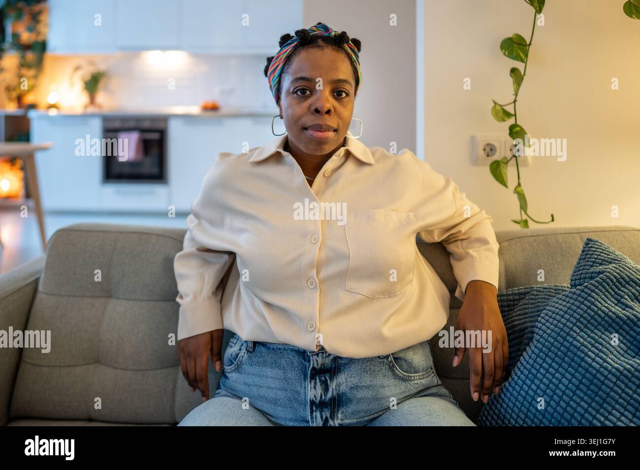 Femme afro-américaine sûre d'elle s'assoit confortablement sur le canapé regardant la caméra avec une expression calme. Acceptation de soi, positivité corporelle, confiance, Banque D'Images