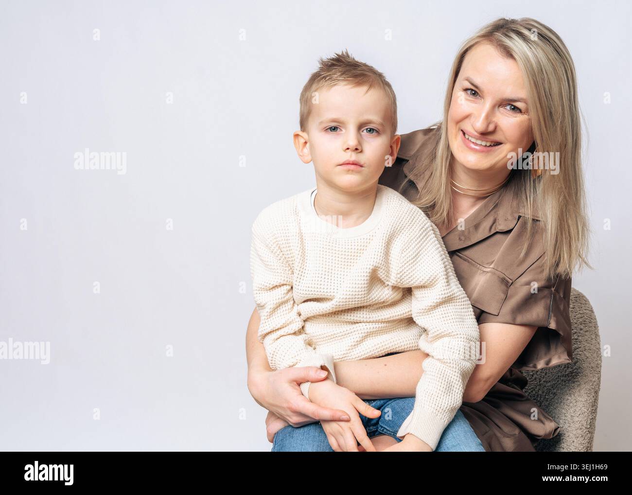 Garçon de 4-5 ans assis sur les genoux de sa mère maman souriant et le garçon n'est pas satisfait, à la fois l'apparence européenne garçon blond avec les yeux bleus, studio Banque D'Images
