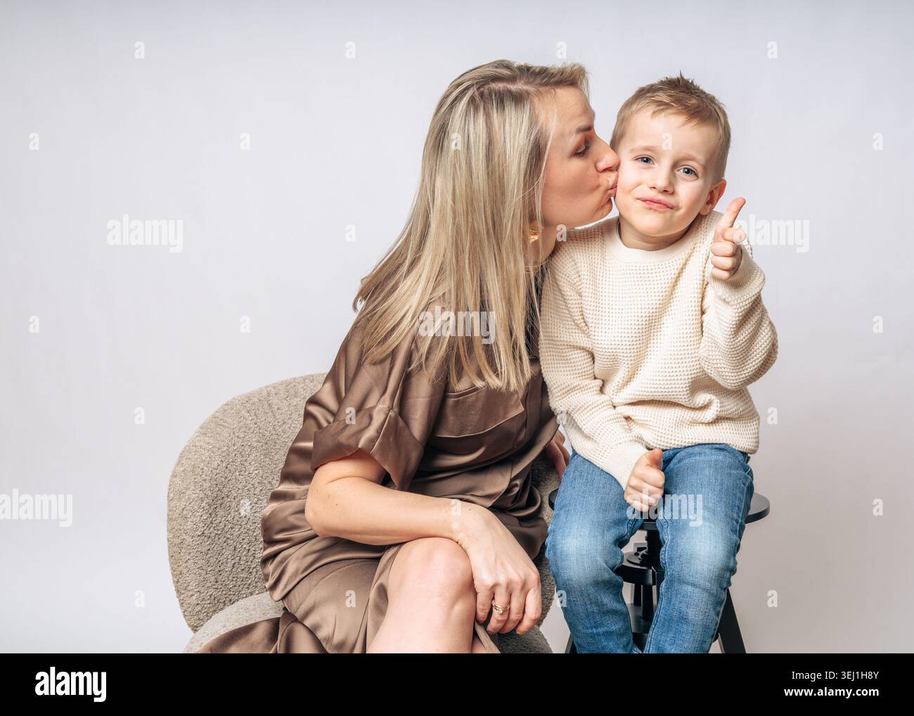 Maman embrasse un garçon de 4-5 ans sur la joue, le garçon sourit et montre une classe de doigt, à la fois un garçon blond d'apparence européenne avec des yeux bleus, tournage en studio Banque D'Images