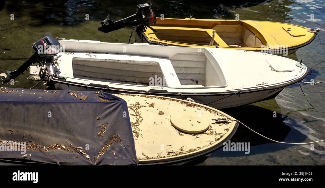 Petits bateaux à moteur hors-bord amarrés ensemble sur la surface de l'eau calme près de la côte à Opatija, en Croatie, couverts de feuilles mortes et de brindilles. Banque D'Images