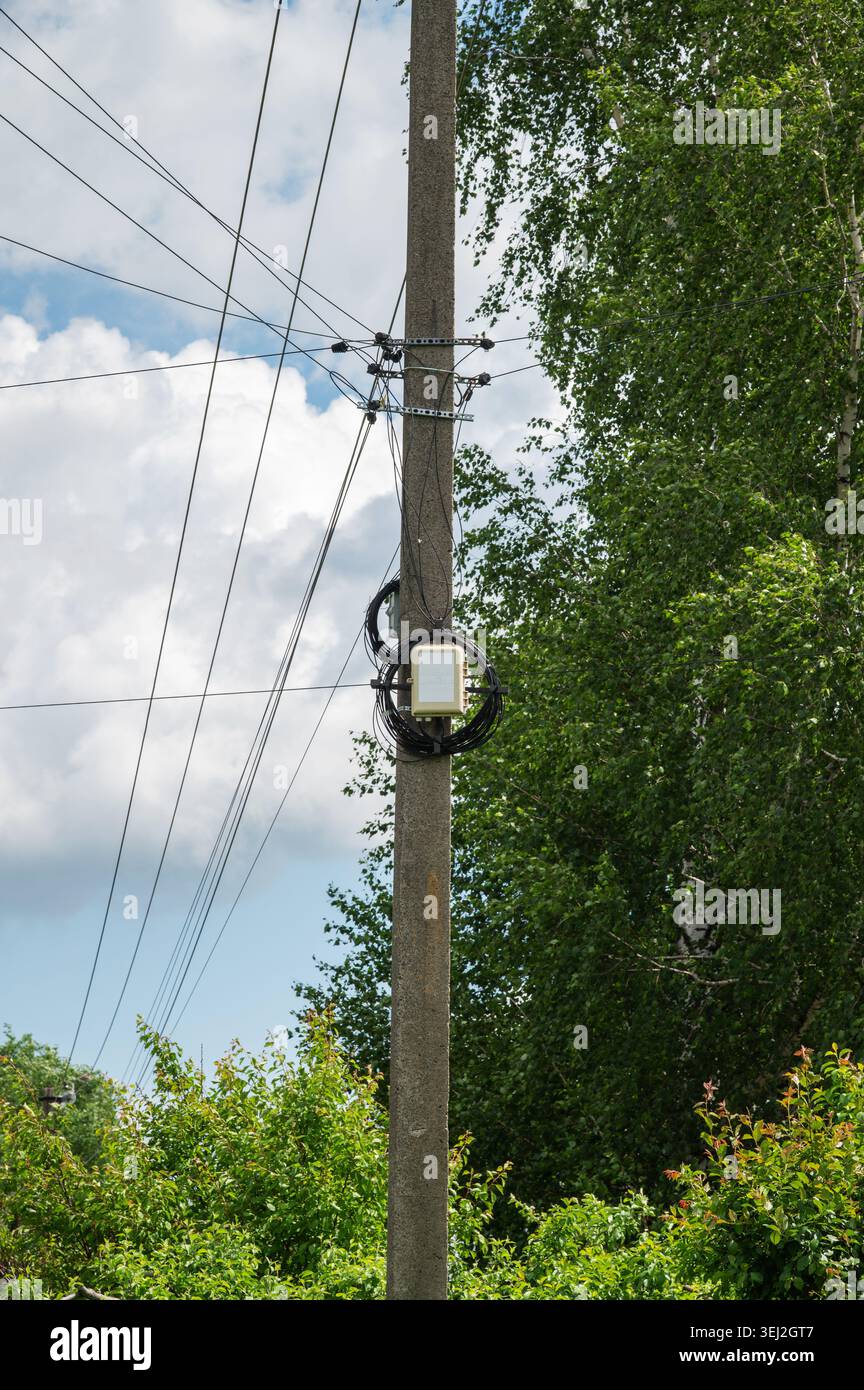 Poteau de service avec lignes électriques aériennes à côté d'arbres verts d'été Banque D'Images