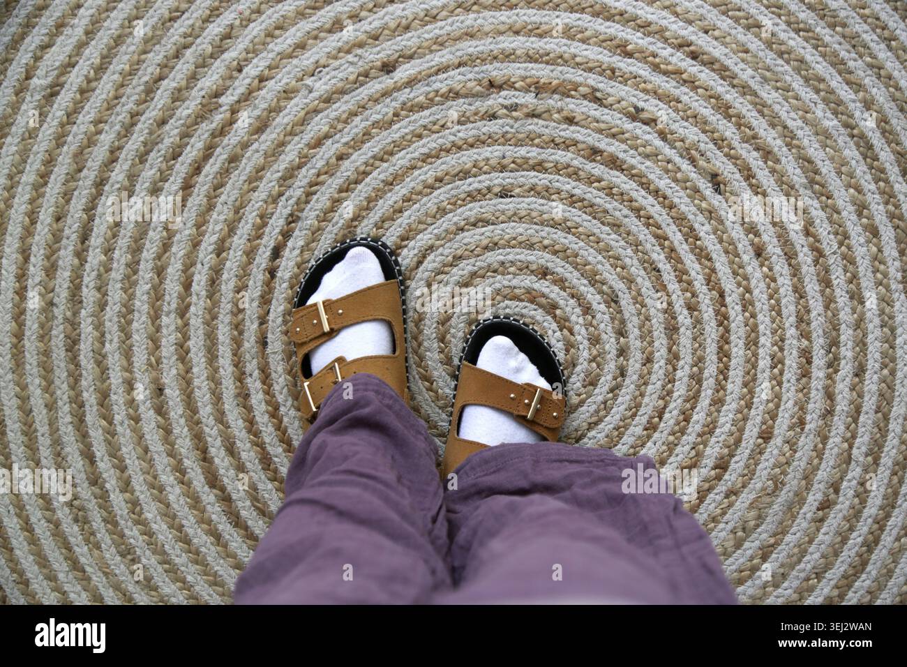Vue de dessus des sandales pour enfants en daim crème portées avec des chaussettes blanches sur un tapis de jute naturel, détail de mode pour enfants inspiré du boho confortable avec des tons terreux chauds Banque D'Images