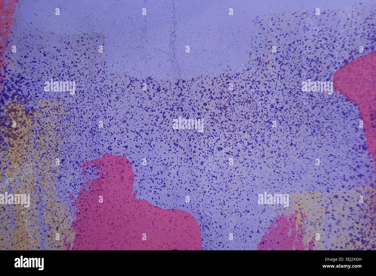 Gros plan d'un mur urbain recouvert d'éclaboussures de peinture graffiti chaotiques et de motifs de pulvérisation dans des tons violets, roses et bleus vifs. Banque D'Images