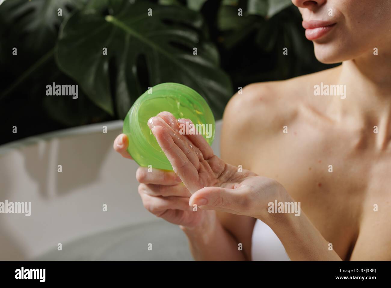 Une femme applique le gel d'aloe vera sur sa main, mettant en valeur les routines de soins de la peau dans un environnement serein rempli de verdure luxuriante, parfait pour la beauté et le bien Banque D'Images