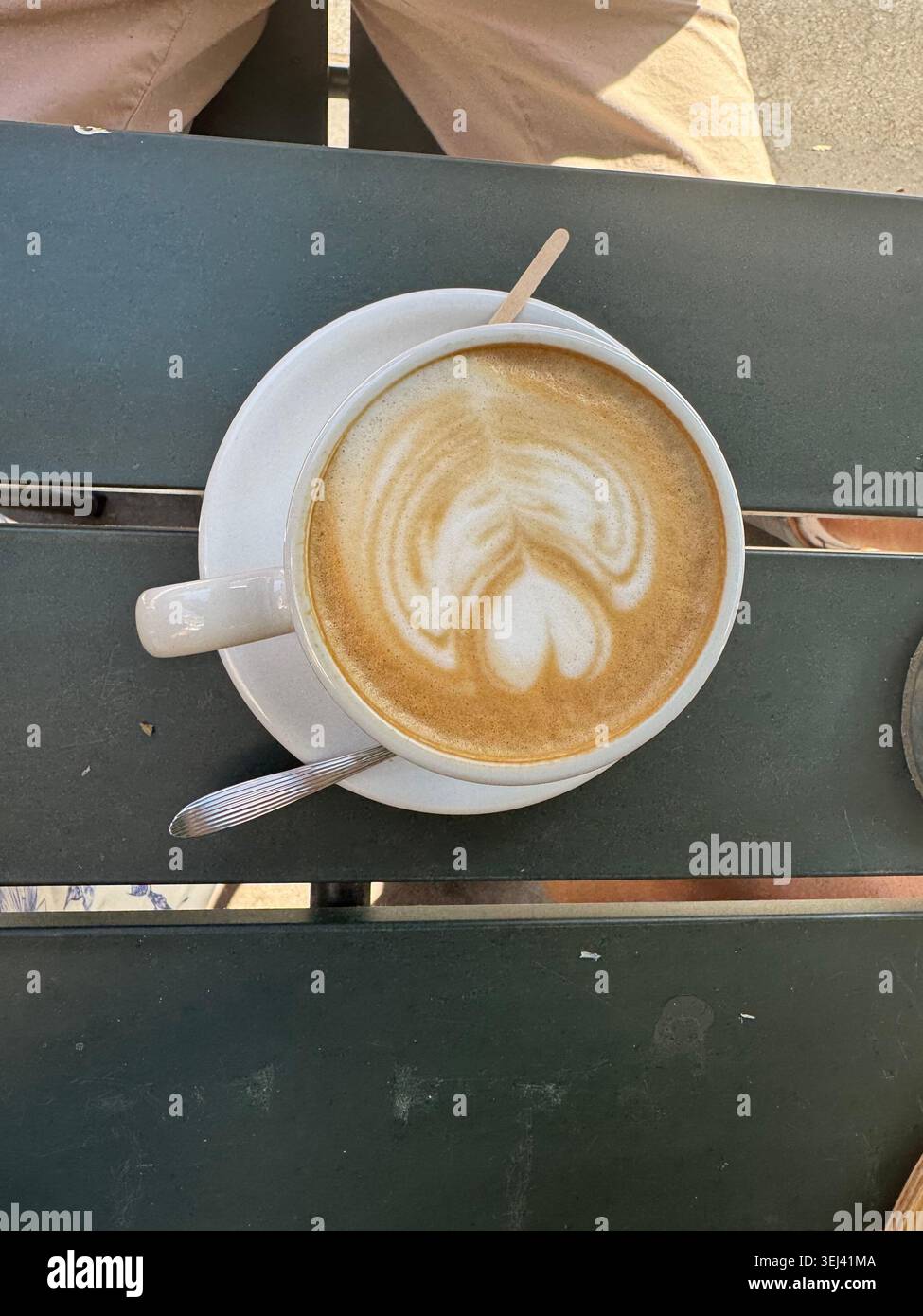 Une vue de dessus directe d'une tasse en céramique blanche remplie d'un cappuccino chaud montrant un magnifique design d'art latte en forme de coeur sur une table en bois. - Image de stock capturée avec un smartphone