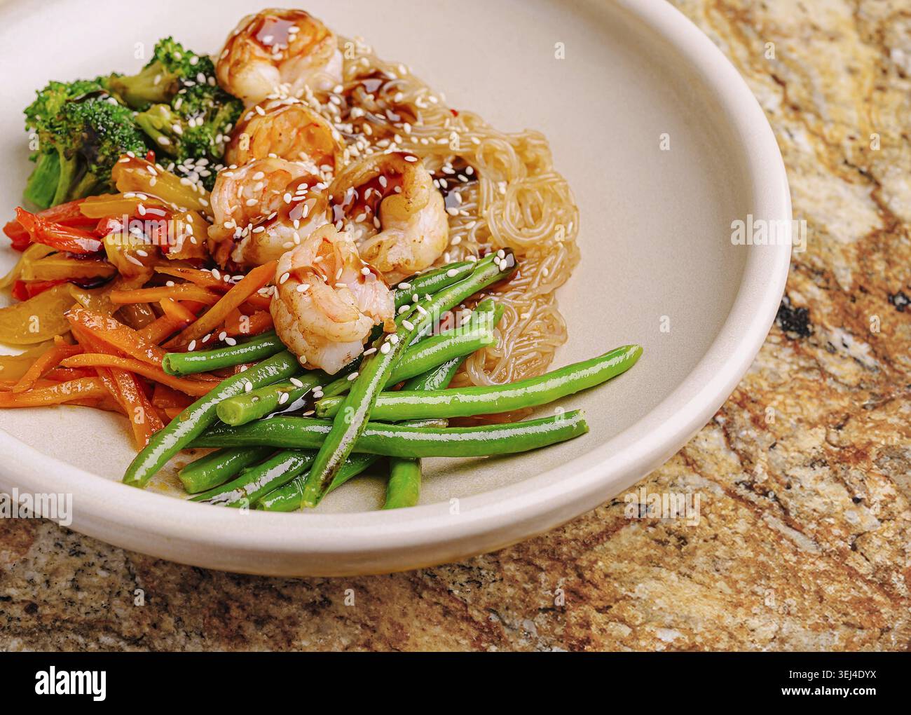 Nourriture, crevettes sautées servies avec des nouilles claires et des légumes vibrants comme le brocoli et les haricots verts. Le plat est présenté élégamment sur un col neutre Banque D'Images