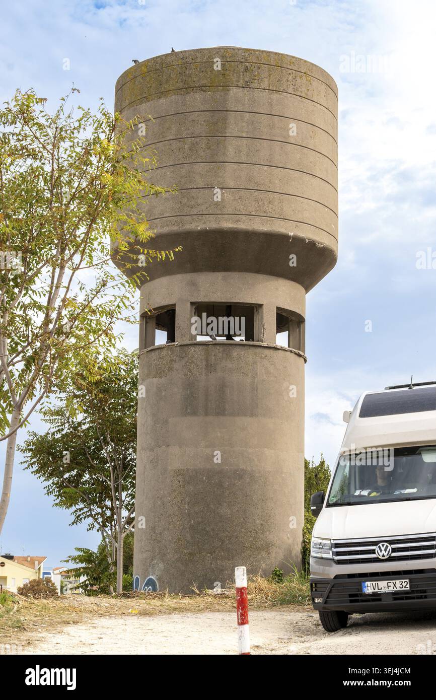 Vieste - Pouilles - Italie - 08-29-2025 : vue en angle bas d'un château d'eau en béton avec de petits oiseaux, des arbres et un camping-car garé avec emblème sous SC Banque D'Images