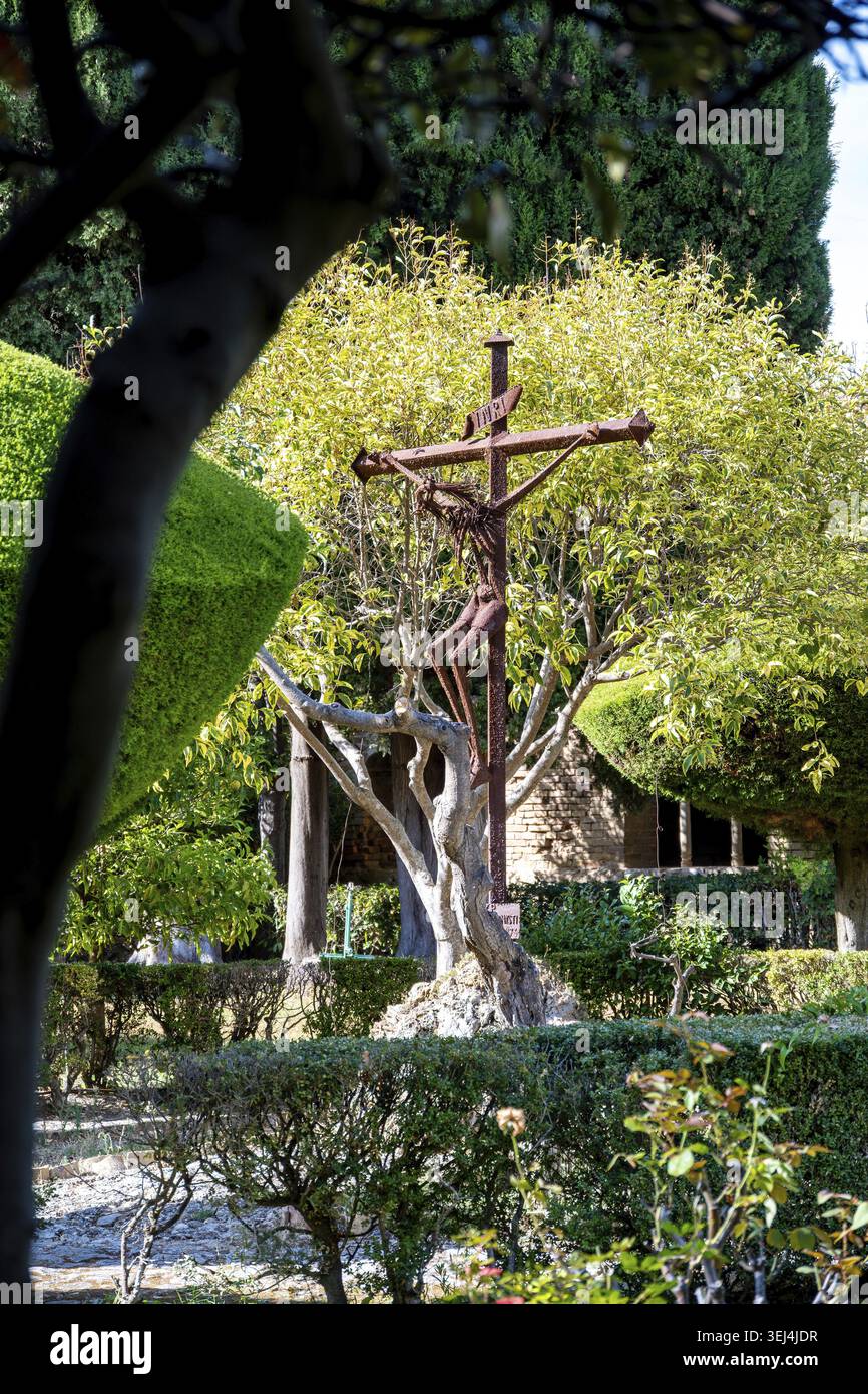 Vieste - Pouilles - Italie - 29-08-2025 : sculpture crucifix en métal rouillé dans un jardin bien entretenu, encadré par des arbres et des haies, avec un bâtiment en pierre A. Banque D'Images