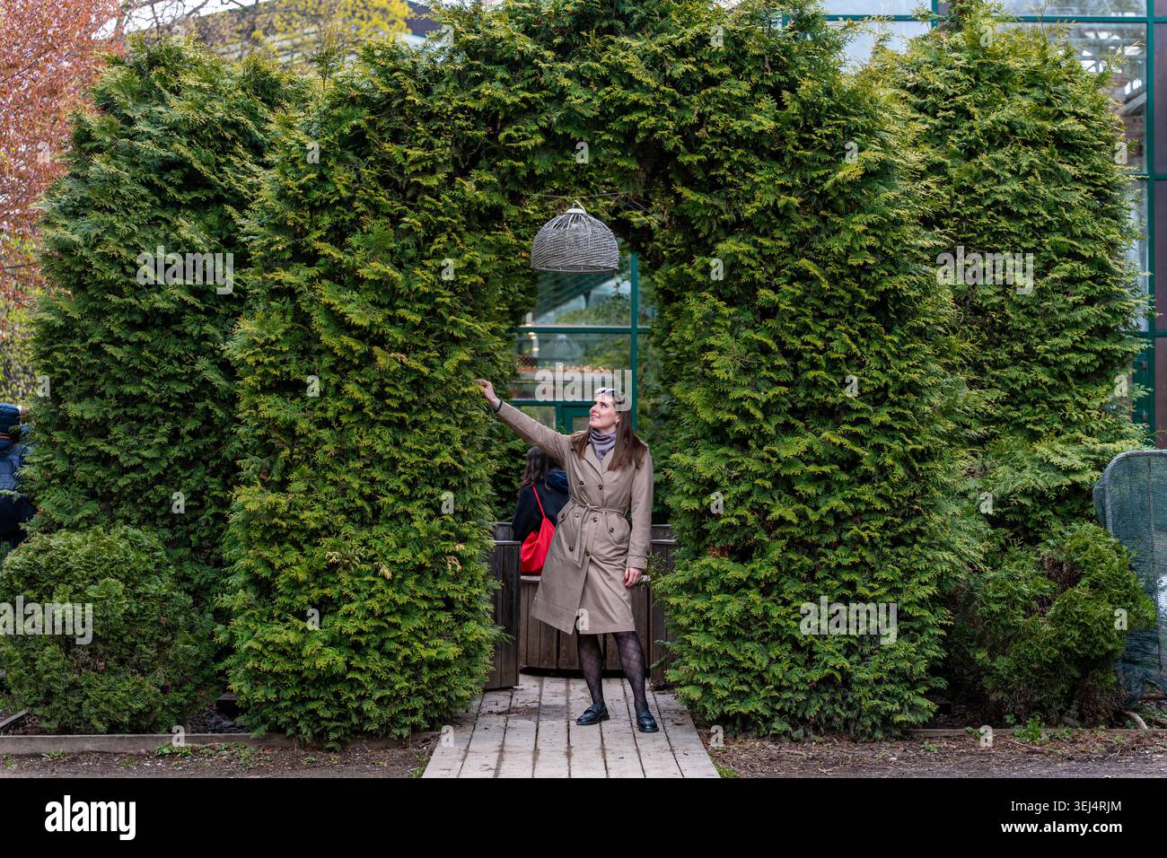 Femme atteignant l'anneau de la fontaine de l'eau alors qu'elle était assise geste ludique capturé Midsplash, manteau drapé, Hedge Arch décoré scène, Candid Banque D'Images
