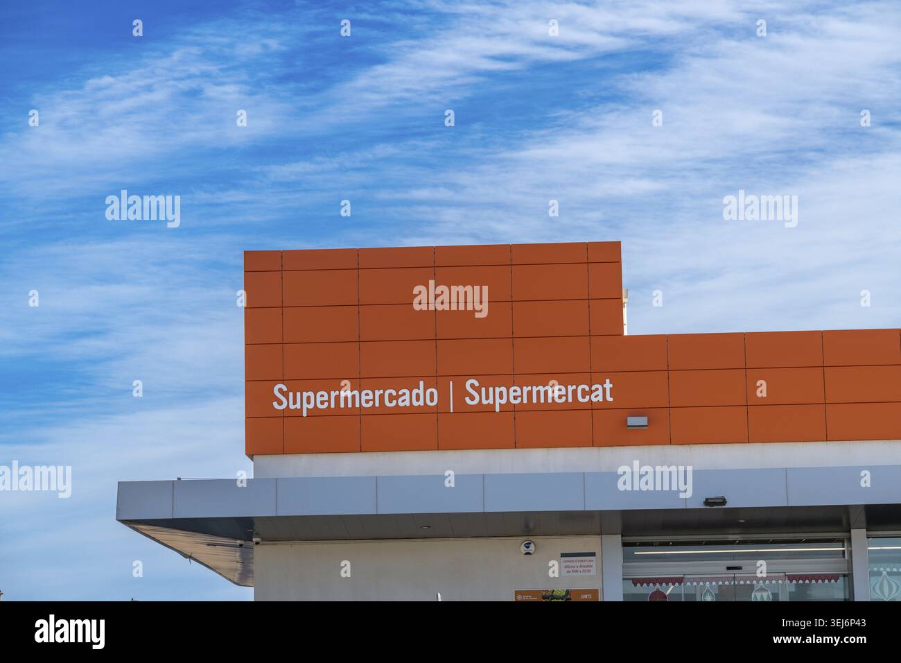 Els Poblets - Communauté valencienne - Espagne - 12-06-2025 : façade orange avec les mots Supermercado | Supermercat au-dessus d'une verrière grise encadrée par un Banque D'Images