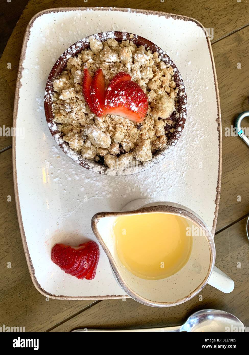 Crumble de fruits chaud garni de fraises fraîches et d'un saupoudrage de sucre glace servi avec une crème anglaise crémeuse dans le Northampton Northamptonshire UK - Image de stock capturée avec un smartphone