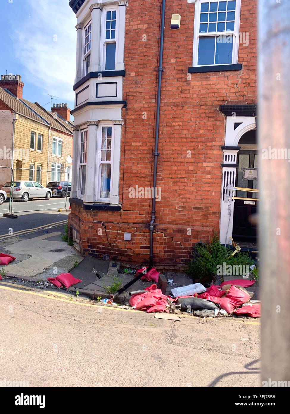 Maison d'angle en briques rouges dans une rue résidentielle de Northampton en Angleterre avec des sacs de sable et des débris placés le long de la base indiquant des travaux de réparation des inondations - Image de stock capturée avec un smartphone