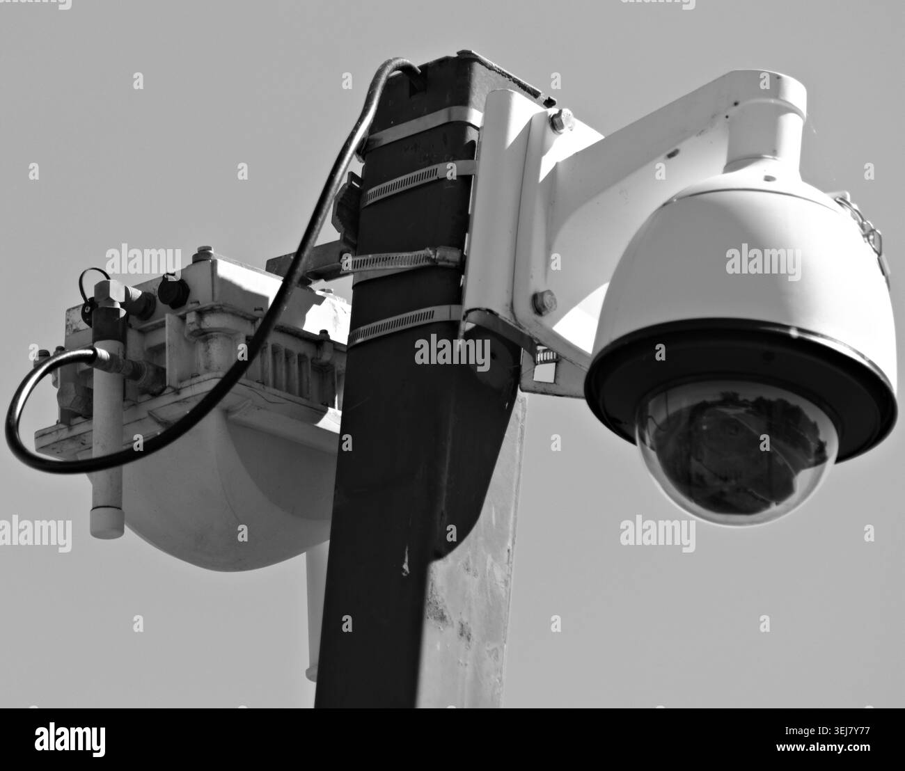 Gros plan d'une caméra de sécurité montée sur poteau et d'un équipement de surveillance contre un ciel bleu clair Banque D'Images