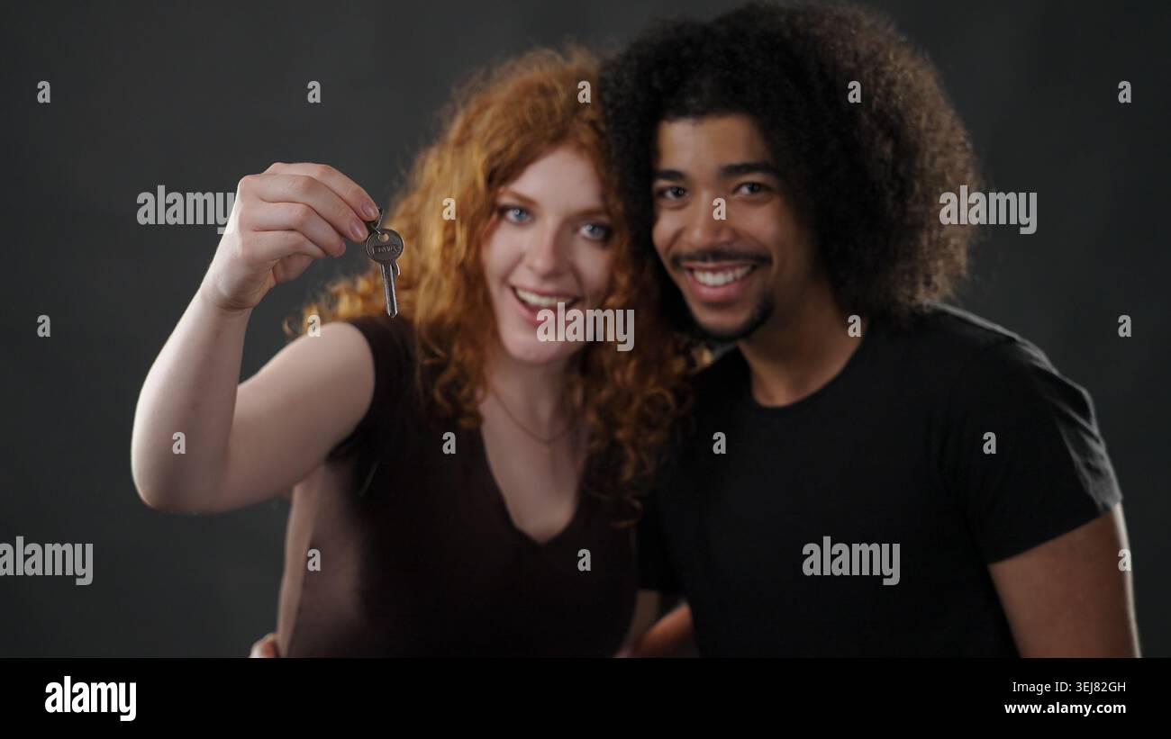 Heureux couple diversifié tenant les clés de la maison célébrant la propriété de la maison Banque D'Images