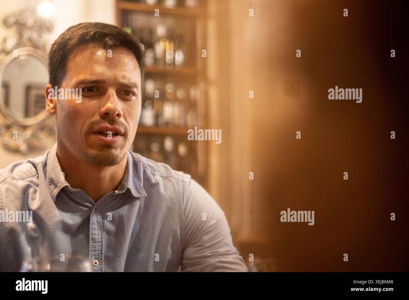 Jeune homme ayant une conversation émotionnelle ou sérieuse lors d'un dîner dans un restaurant confortable. ECLAIRAGE d'ambiance chaleureux et expression faciale franche cr Banque D'Images