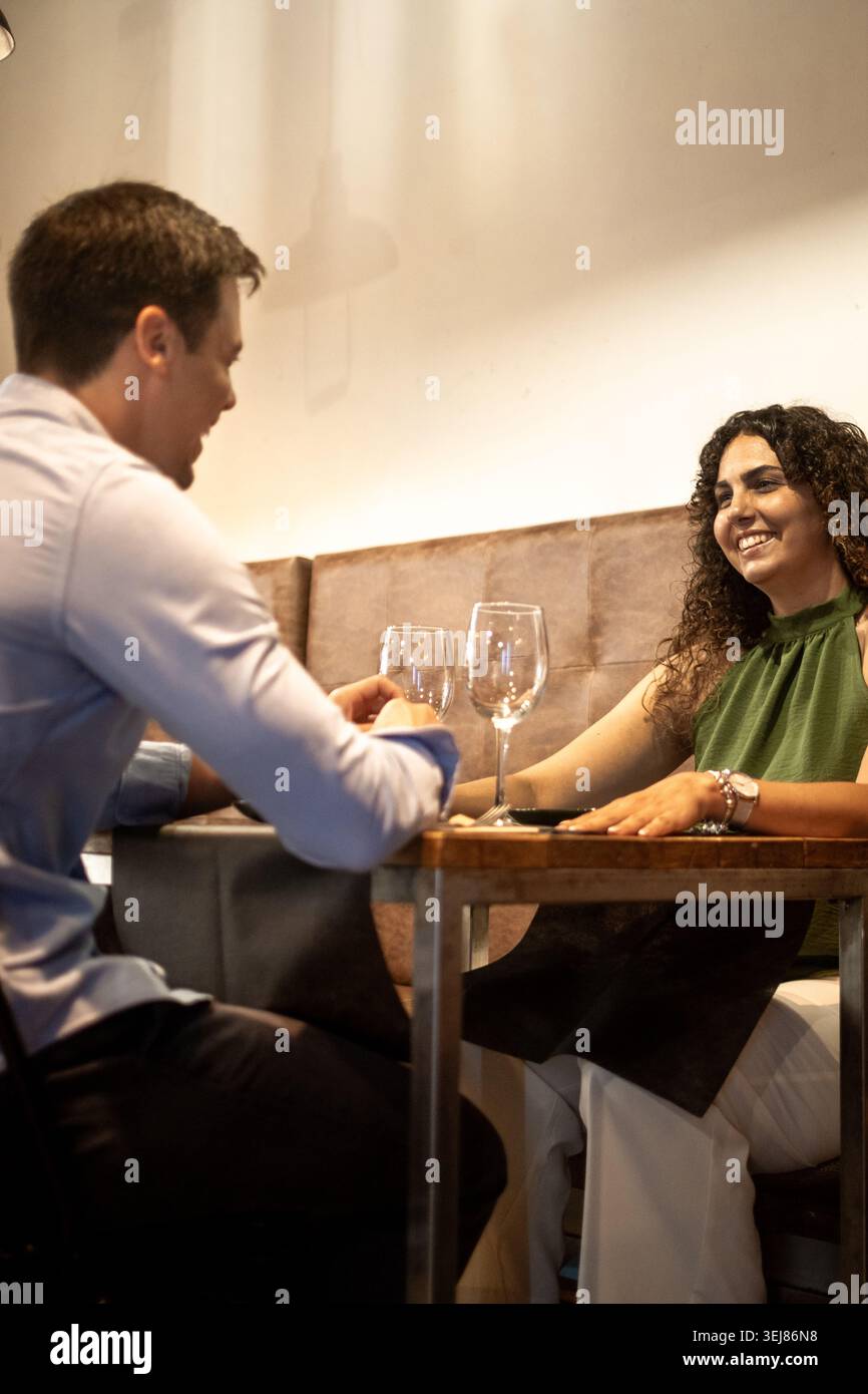 Jeune couple souriant et profitant d'un dîner détendu dans un restaurant confortable. Éclairage ambiant chaleureux, vêtements élégants et décontractés et interaction authentique Banque D'Images