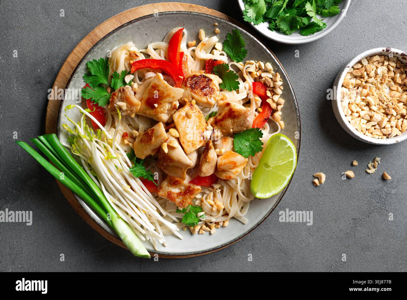 Nouilles thaïlandaises authentiques au poulet nappées de cacahuètes écrasées, de germes de haricots, de coriandre et de citron vert. Repas thaïlandais, nouilles de poulet sautées sur béton Banque D'Images