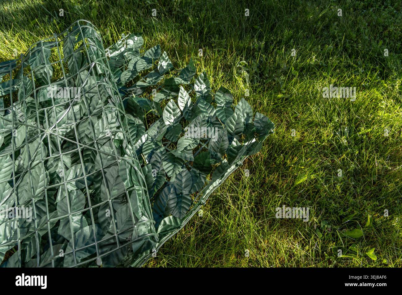 Feuilles de lierre en plastique artificiel placées sur la pelouse, une clôture artificielle à attacher à la clôture, clôture de la parcelle voisine, panneaux de lea en plastique Banque D'Images