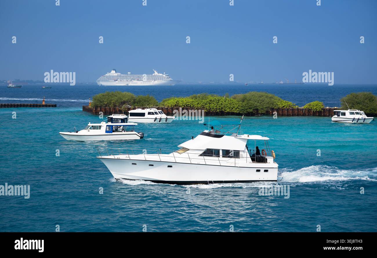 Une photographie de jour d'une voie navigable côtière animée avec plusieurs yachts à moteur blancs et hors-bord naviguant dans une eau turquoise vibrante. Dans le Banque D'Images