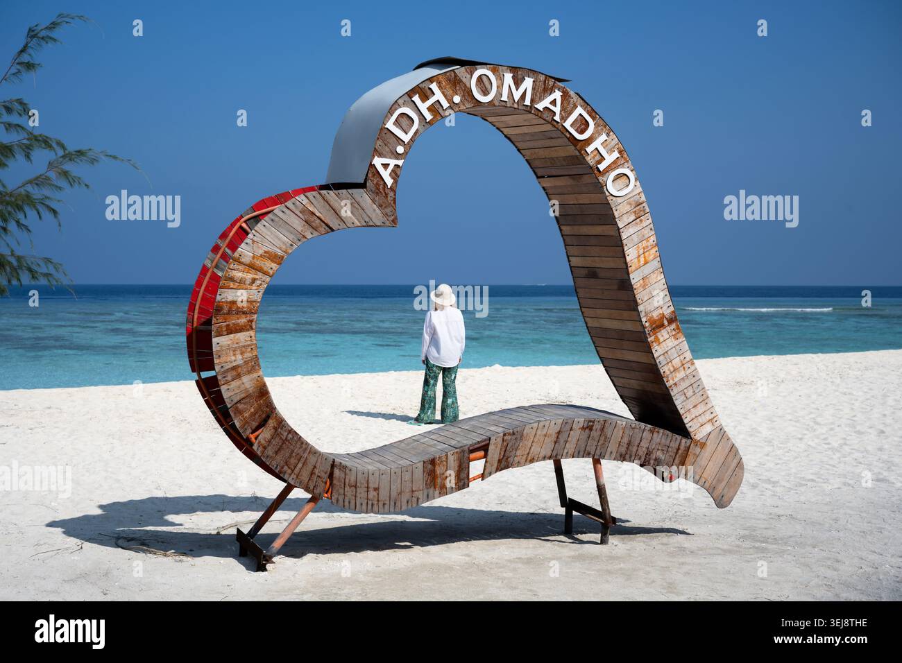 Photographie d'une plage tropicale avec une grande structure rustique en bois en forme de cœur reposant sur du sable blanc. La structure a le texte blanc 'A.DH Banque D'Images