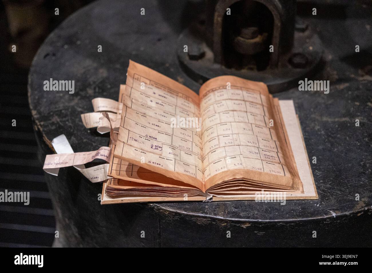 Un livre de grand livre antique contenant des documents financiers manuscrits repose sur une base circulaire de machinerie en fer. Banque D'Images