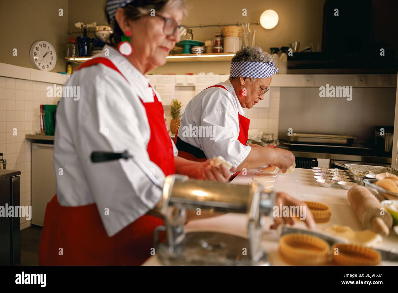 Chefs femmes caucasiennes et noires actives préparant des pâtisseries dans un cadre de cuisine professionnel. Banque D'Images
