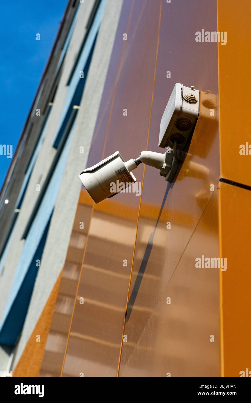 Une caméra de surveillance moderne montée sur un bâtiment urbain reflétant le ciel clair et les couleurs vives de la façade, exposant la sécurité et la technologie I. Banque D'Images