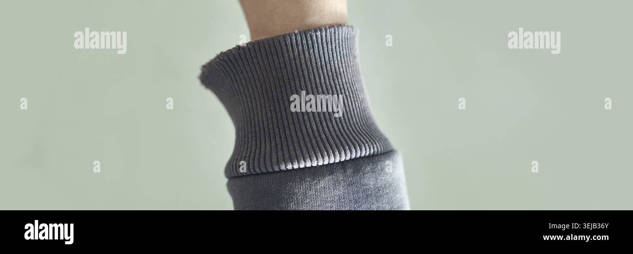 Gros plan confortable de tissu tricoté gris doux sur bras relevé sur fond vert Banque D'Images